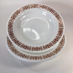 May include: Two white ceramic bowls with a brown floral pattern around the rim. The bowls are stacked on top of each other. The top bowl is deeper than the bottom bowl.