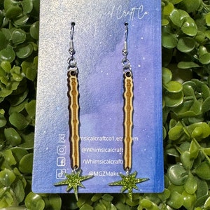 May include: A pair of wooden earrings with a brown and white striped design and a green glitter star charm. The earrings are on a white card with the text "Whimsicalcraftco.etsy.com @Whimsicalcraft /Whimsicalcraft @MGZMakes".