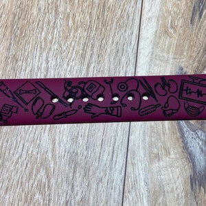 May include: A maroon watch band with black etched medical-themed illustrations. The band features images of a brain, bones, medical tools, and organs. The band has multiple holes for adjustment.