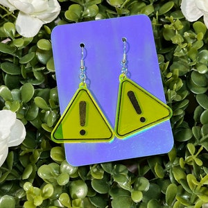 May include: A pair of yellow triangle-shaped earrings with an exclamation point in the center. The earrings are on a blue background.