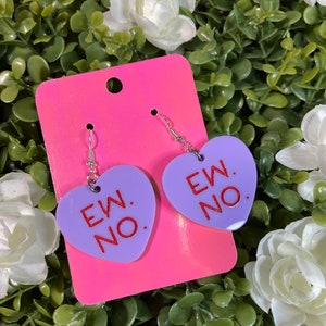 May include: A pair of purple heart-shaped earrings with silver hooks. The hearts have the text "EW. NO." written in red.