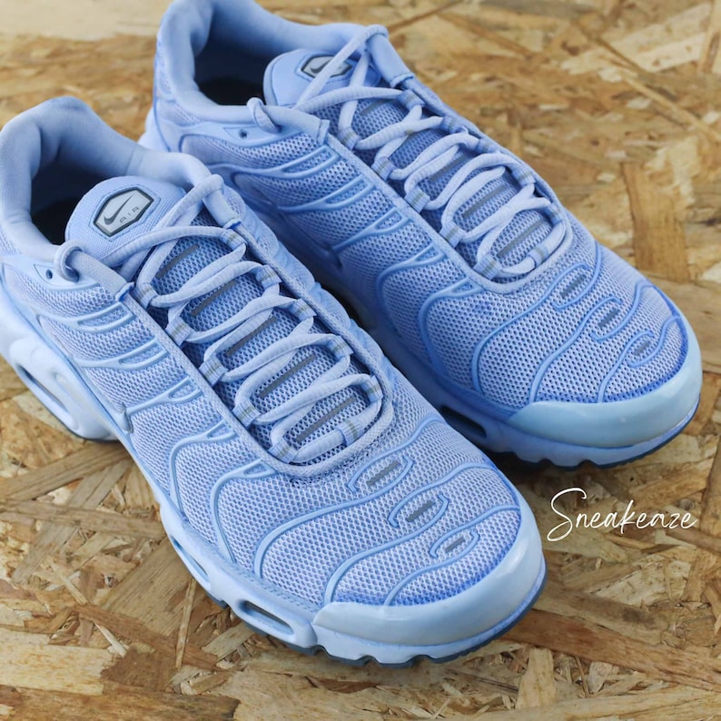 May include: A pair of light blue Nike Air Max Plus sneakers with a mesh upper and a white swoosh logo. The sneakers have a white midsole and a black outsole.