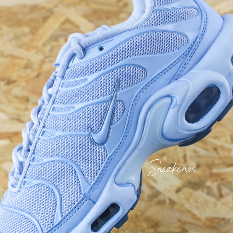 May include: A light blue Nike Air Max Plus sneaker with a mesh upper and a silver Swoosh logo. The shoe has a white midsole and a black outsole.