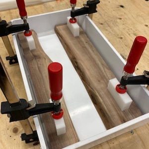 Może przedstawiać: Biała plastikowa taca z dwoma kawałkami drewna w środku, zaciśniętymi czerwonymi klamrami. Drewno jest utrzymywane na miejscu przez białe klocki.