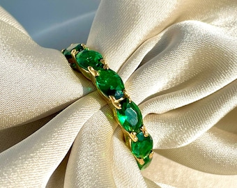 May include: A gold ring with a band of emerald green oval-shaped stones.