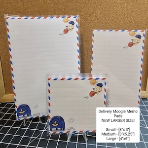 Op de afbeelding: Delivery Moogle memoblokken in drie maten: klein (7,6 cm x 7,6 cm), medium (7,6 cm x 13,3 cm) en groot (10,2 cm x 15,2 cm). Elk blok heeft gelijnd wit papier, een rood-wit-blauwe rand en een cartoon bezorgfiguur.
