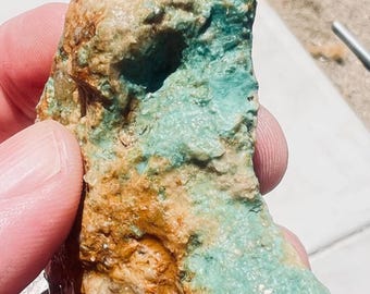 Pode incluir: Fragmento de rocha bruta com um contraste de cores marcante. A pedra apresenta manchas de turquesa vibrante e tons castanhos terrosos, criando uma textura natural visualmente atraente. A superfície da rocha é irregular.
