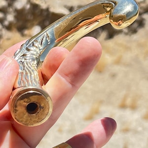 May include: A gold-toned metal walking stick handle with a detailed floral design. The handle is curved and has a smooth, polished finish.