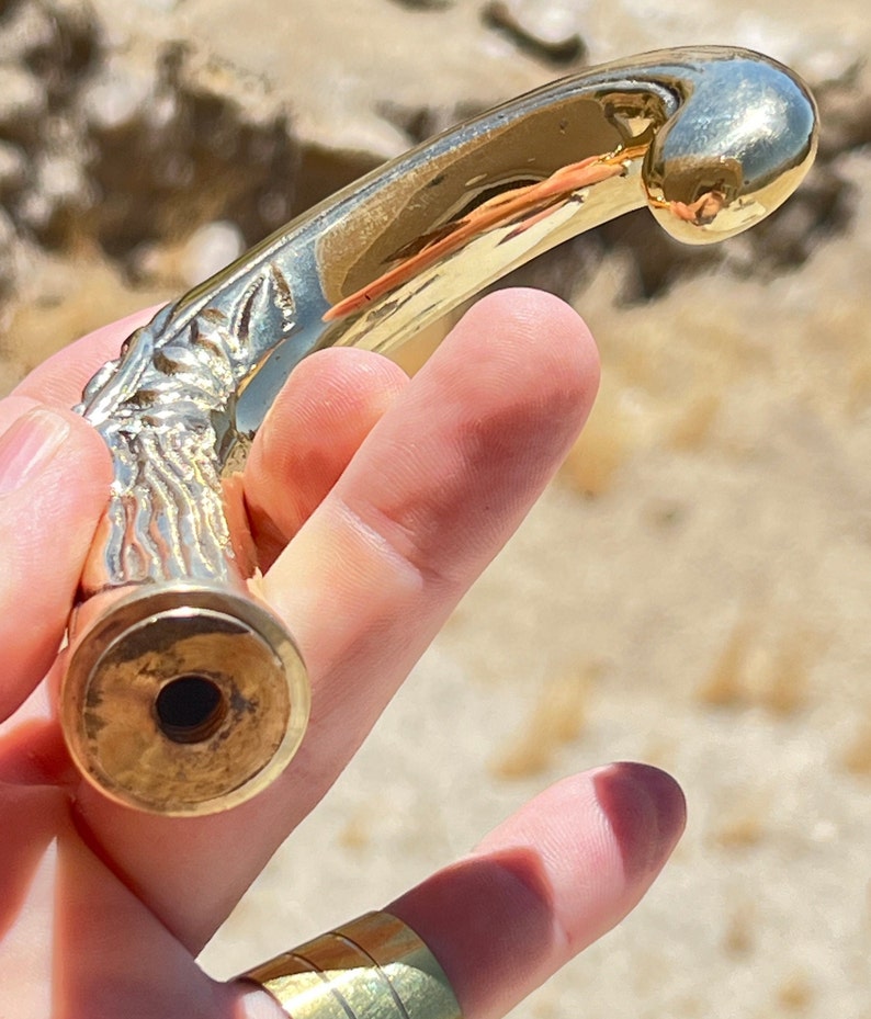 May include: A gold-toned metal walking stick handle with a detailed floral design. The handle is curved and has a smooth, polished finish.