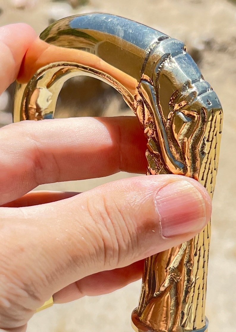 May include: A gold-colored walking stick handle with intricate carvings. The handle is shaped like a curved branch with a detailed design.