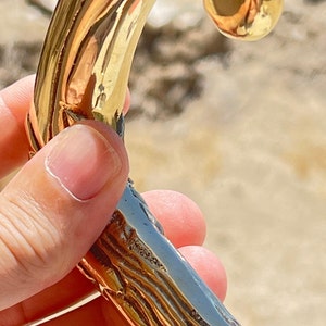 May include: A gold-colored walking stick handle with a detailed, textured design. The handle is curved and has a smooth, polished finish.