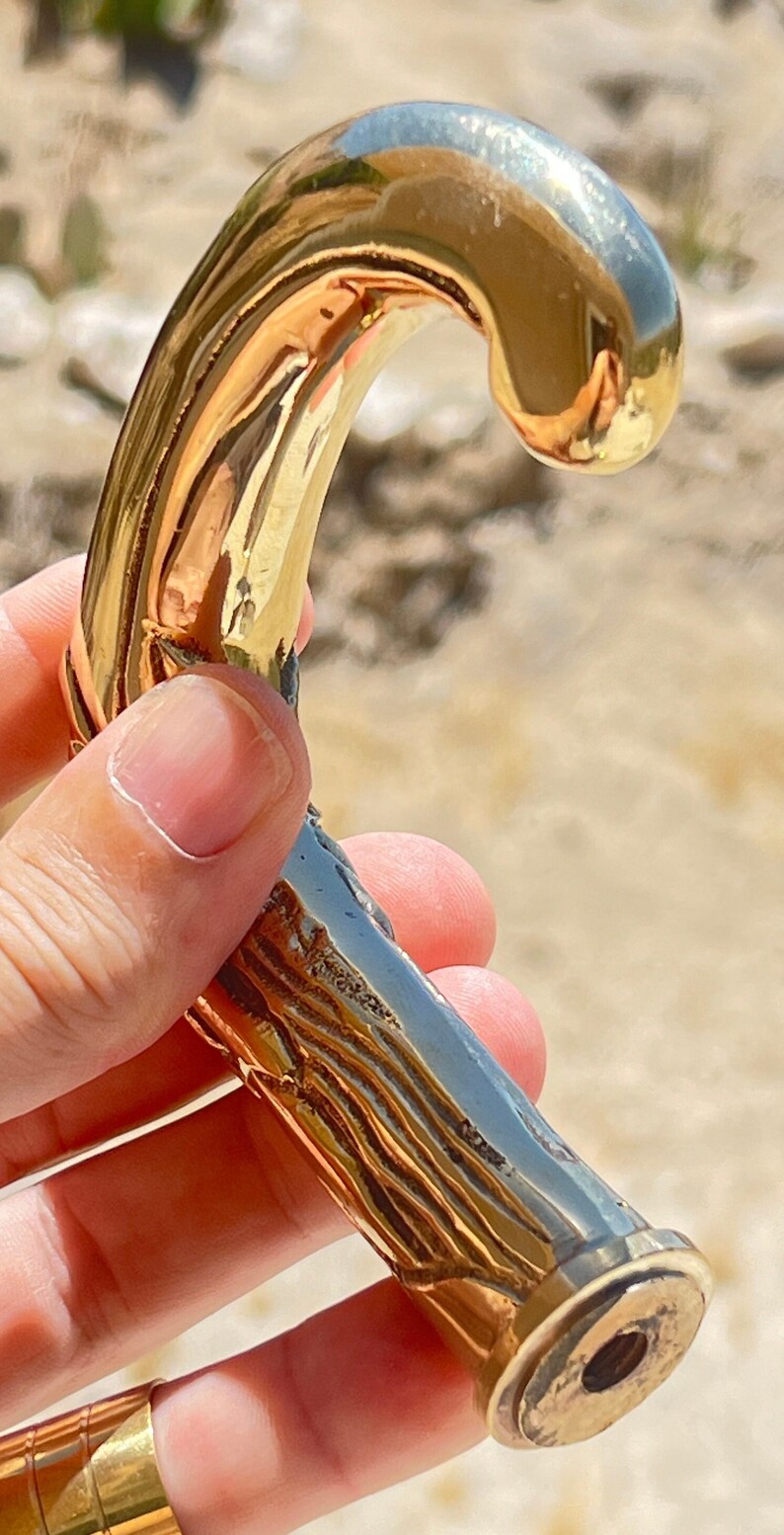 May include: A gold-colored walking stick handle with a detailed, textured design. The handle is curved and has a smooth, polished finish.