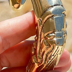 May include: A gold-colored metal door handle with an intricate design. The handle is shaped like a curved hook with a detailed, textured surface.