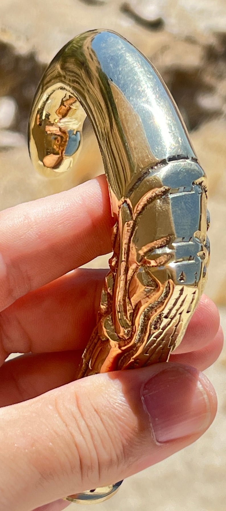 May include: A gold-colored metal door handle with an intricate design. The handle is shaped like a curved hook with a detailed, textured surface.