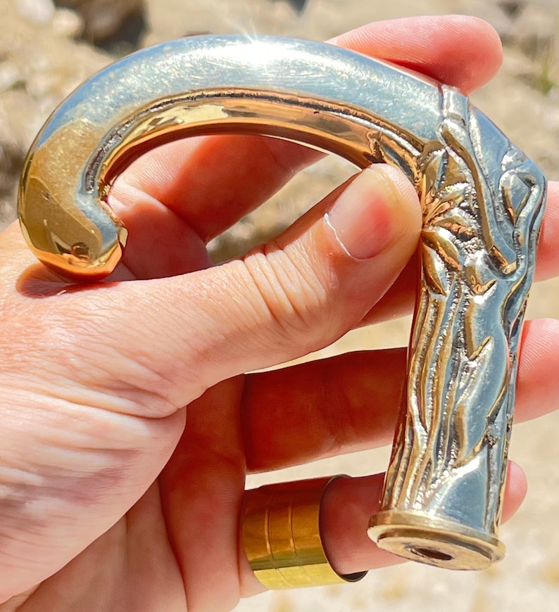 May include: A gold-toned metal walking stick handle with an ornate design. The handle is shaped like a curved hook and has a detailed floral pattern.