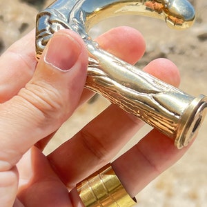 May include: A gold-toned metal walking stick handle with a detailed, textured design. The handle is shaped like a curved branch with a rounded top.
