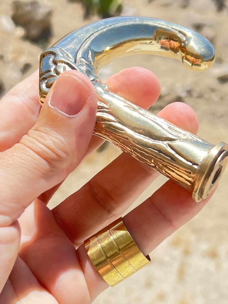 May include: A gold-toned metal walking stick handle with a detailed, textured design. The handle is shaped like a curved branch with a rounded top.