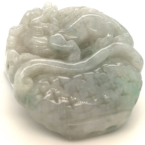 May include: A white jade carving of a dragon, intricately detailed with a curled tail and a raised head. The jade has a translucent quality and a subtle green hue.