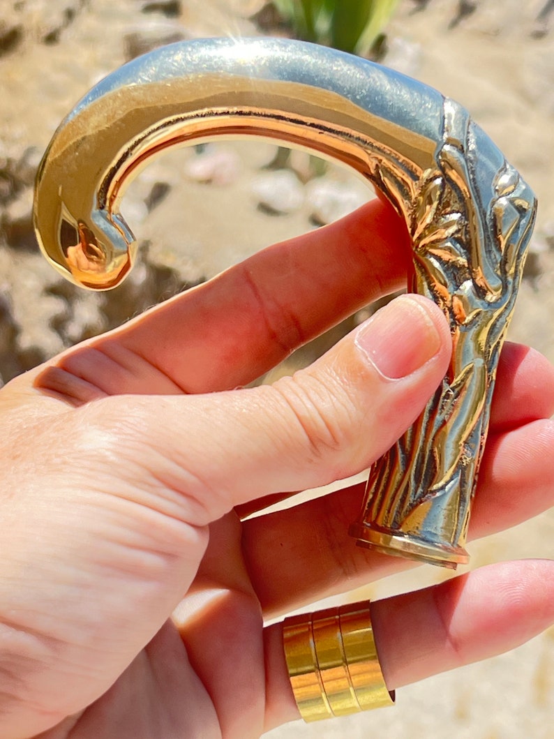 May include: A gold-toned metal cane handle with an ornate design. The handle is shaped like a hook and has a textured surface.