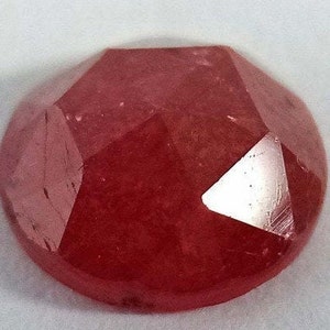 Könnte beinhalten: Ein tief roter Edelstein mit einem facettierten Schliff. Der Edelstein ist rund und hat eine glatte, polierte Oberfläche.