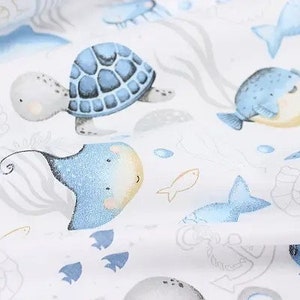 May include: White fabric with a repeating pattern of sea creatures. The design includes a blue sea turtle, stingray, and fish, along with seashells and anchors. The illustrations have a watercolor style.