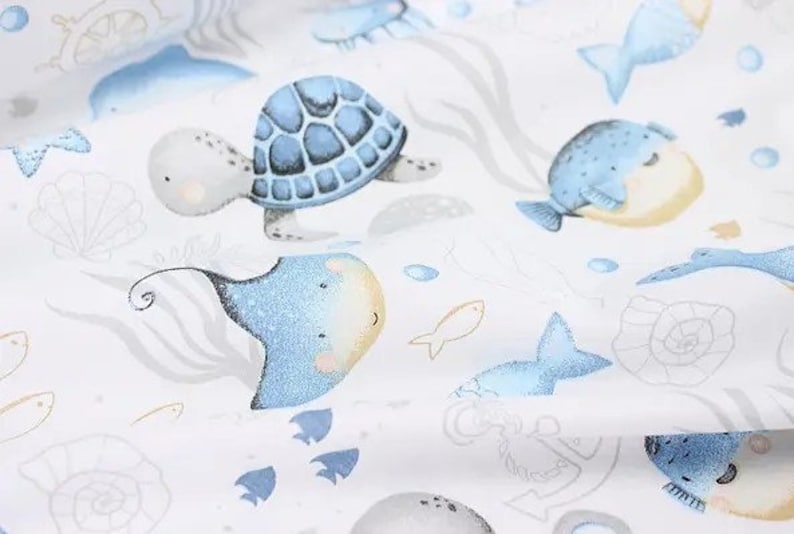May include: White fabric with a repeating pattern of sea creatures. The design includes a blue sea turtle, stingray, and fish, along with seashells and anchors. The illustrations have a watercolor style.