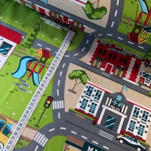 May include: A colorful fabric with a city scene design. The fabric features a fire station, a police station, a playground, and roads with crosswalks. The fabric is printed with a measuring tape, showing the fabric is 33 inches long.