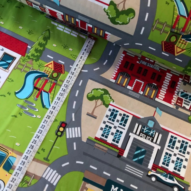 May include: A colorful fabric with a city scene design. The fabric features a fire station, a police station, a playground, and roads with crosswalks. The fabric is printed with a measuring tape, showing the fabric is 33 inches long.