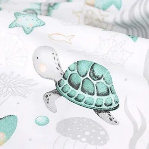 May include: A white fabric with a repeating pattern of sea creatures, including a turtle, starfish, and narwhal. The turtle is the focal point, with a teal shell and light gray body. Other sea life illustrations are in teal and gray.
