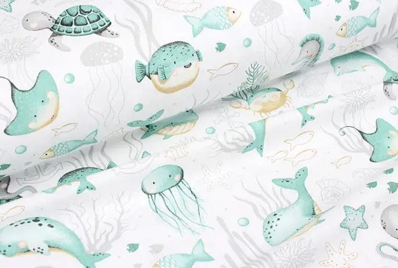 May include: White fabric with an all-over pattern of sea creatures in shades of teal, yellow, and gray. The design includes turtles, fish, jellyfish, and whales, creating a whimsical underwater theme.