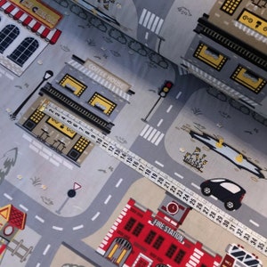 May include: A gray and white fabric with a city scene printed on it. The fabric features buildings, roads, cars, and a fire station. The text "ICE CREAM", "COFFEE HOUSE", and "FIRE STATION" are printed on the fabric.