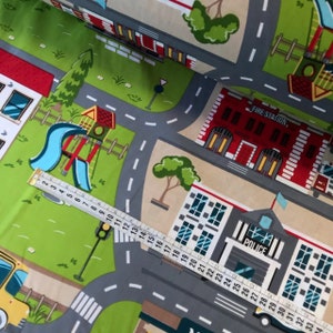 May include: A colorful play mat with a city theme. The mat features a fire station, a police station, a playground, and a road with crosswalks. The mat is made of fabric and is perfect for children to play on.