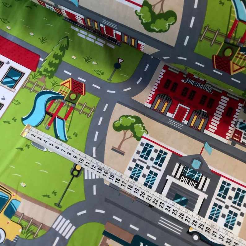 May include: A colorful play mat with a city theme. The mat features a fire station, a police station, a playground, and a road with crosswalks. The mat is made of fabric and is perfect for children to play on.