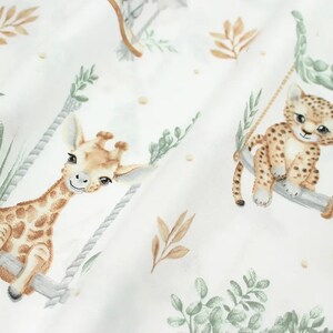 May include: White fabric with a repeating pattern of giraffes and leopards on swings. The animals are illustrated in a watercolor style with brown, tan, and green colors.