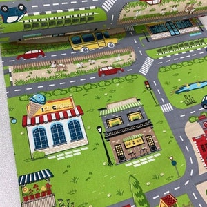 May include: A colorful fabric featuring a play mat design with a town scene. The fabric includes a bus, cars, a coffee house, an ice cream shop, a pond, and a small market. The fabric is gray, green, brown, red, yellow, and blue.