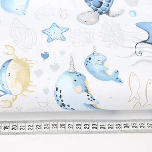 May include: White fabric with a repeating pattern of sea creatures in blue and gold. The design includes narwhals, crabs, starfish, and fish. A ruler with inch measurements is along the bottom.