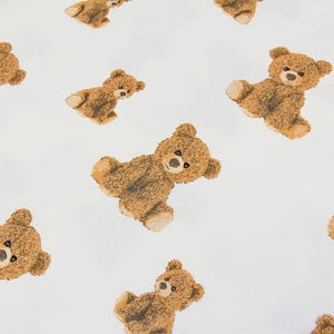 May include: White fabric with a repeating pattern of brown teddy bears. Each bear has a light brown muzzle, dark eyes, and tan paws. The bears are in various poses, creating a playful and whimsical design.