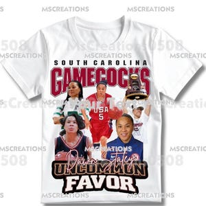 May include: White t-shirt featuring a collage of basketball players and the text "SOUTH CAROLINA GAMECOCKS." The design includes the text "Dawn Staley" and "UNCOMMON FAVOR." The shirt has a crew neck and short sleeves.