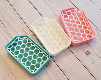 May include: Three soap dishes in different colors: teal, white, and pink. Each dish has a honeycomb design and is made of a durable plastic material.