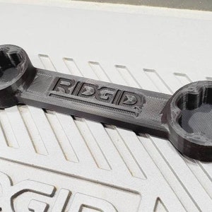 以下が含まれることがあります： ハンドルに「RIDGID」という文字が刻印された黒いプラスチック製のレンチ。レンチは両端に異なるサイズのソケットが2つあります。