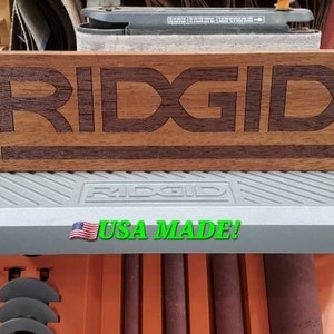 May include: A wooden sign with the word "RIDGID" engraved in it. The sign is sitting on top of a gray machine with the words "RIDGID" and "USA MADE!" printed on it.
