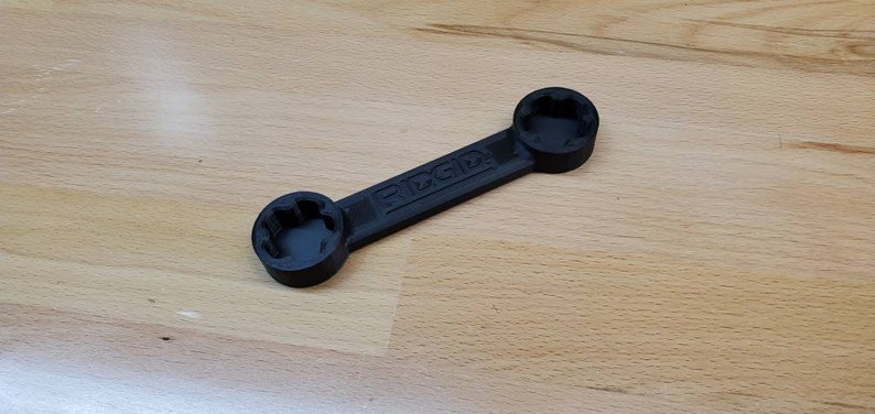 以下が含まれることがあります： 両端にソケットが2つ付いた黒いプラスチック製のレンチ。レンチには「RIGID」と表示されています。