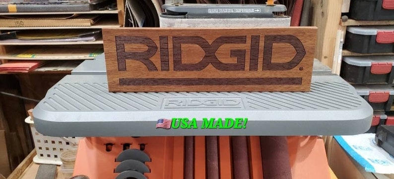 May include: A wooden sign with the word "RIDGID" engraved in it. The sign is sitting on top of a gray machine with the words "RIDGID" and "USA MADE!" printed on it.