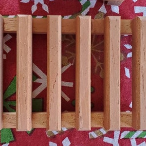 May include: A wooden soap dish with five slats. The dish is made of light brown wood and has a rectangular shape.