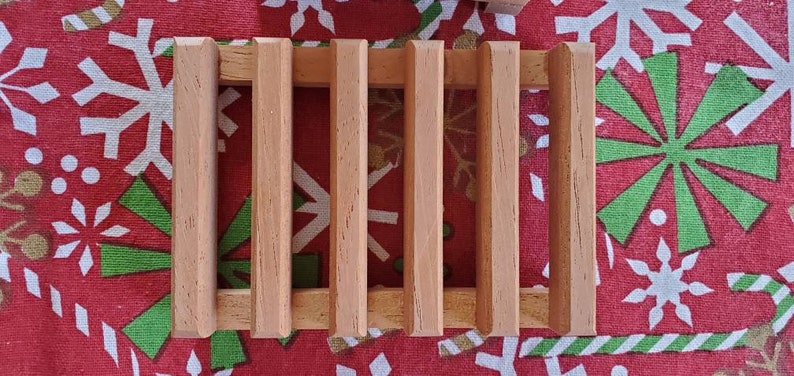 May include: A wooden soap dish with five slats. The dish is made of light brown wood and has a rectangular shape.