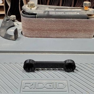 以下が含まれることがあります： 灰色の表面にRIDGIDロゴが付いた黒いレンチ。レンチはナットやボルトの締め付けと緩め用です。