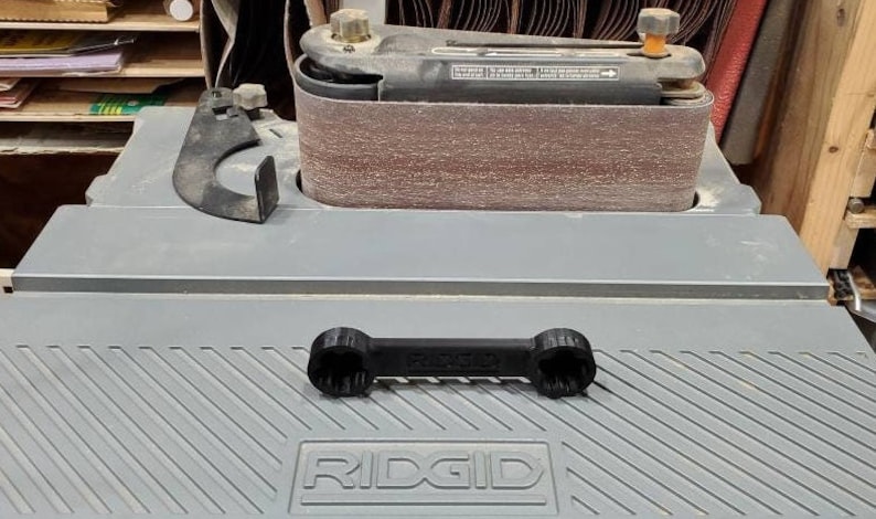 以下が含まれることがあります： 灰色の表面にRIDGIDロゴが付いた黒いレンチ。レンチはナットやボルトの締め付けと緩め用です。