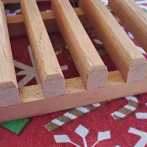 May include: A wooden soap dish with a grid pattern. The dish is made of light brown wood and has a natural finish.
