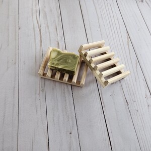 May include: Two wooden soap dishes, one with a green and white bar of soap on top. The dishes are made of natural wood and have a rustic look.