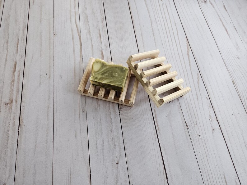 May include: Two wooden soap dishes, one with a green and white bar of soap on top. The dishes are made of natural wood and have a rustic look.